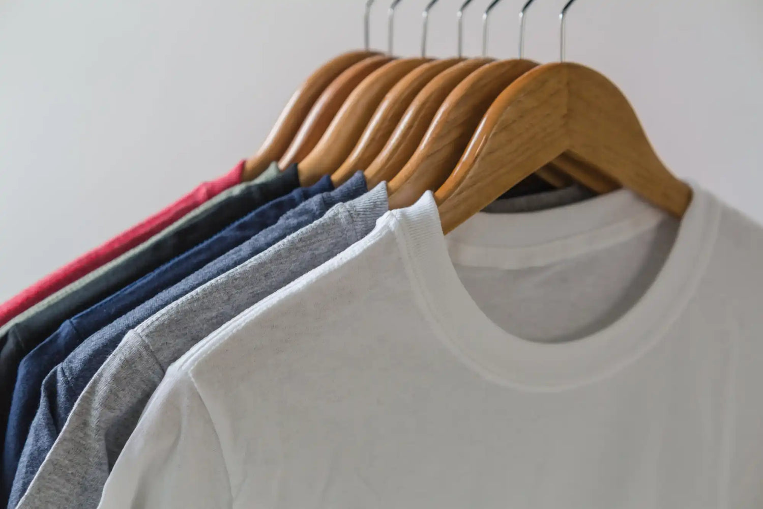 Colorful t-shirts on wooden hangers.